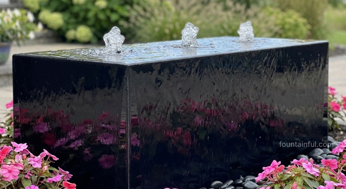 Black acrylic rectangular Heiho fountain with three water plumes, surrounded by pink impatiens